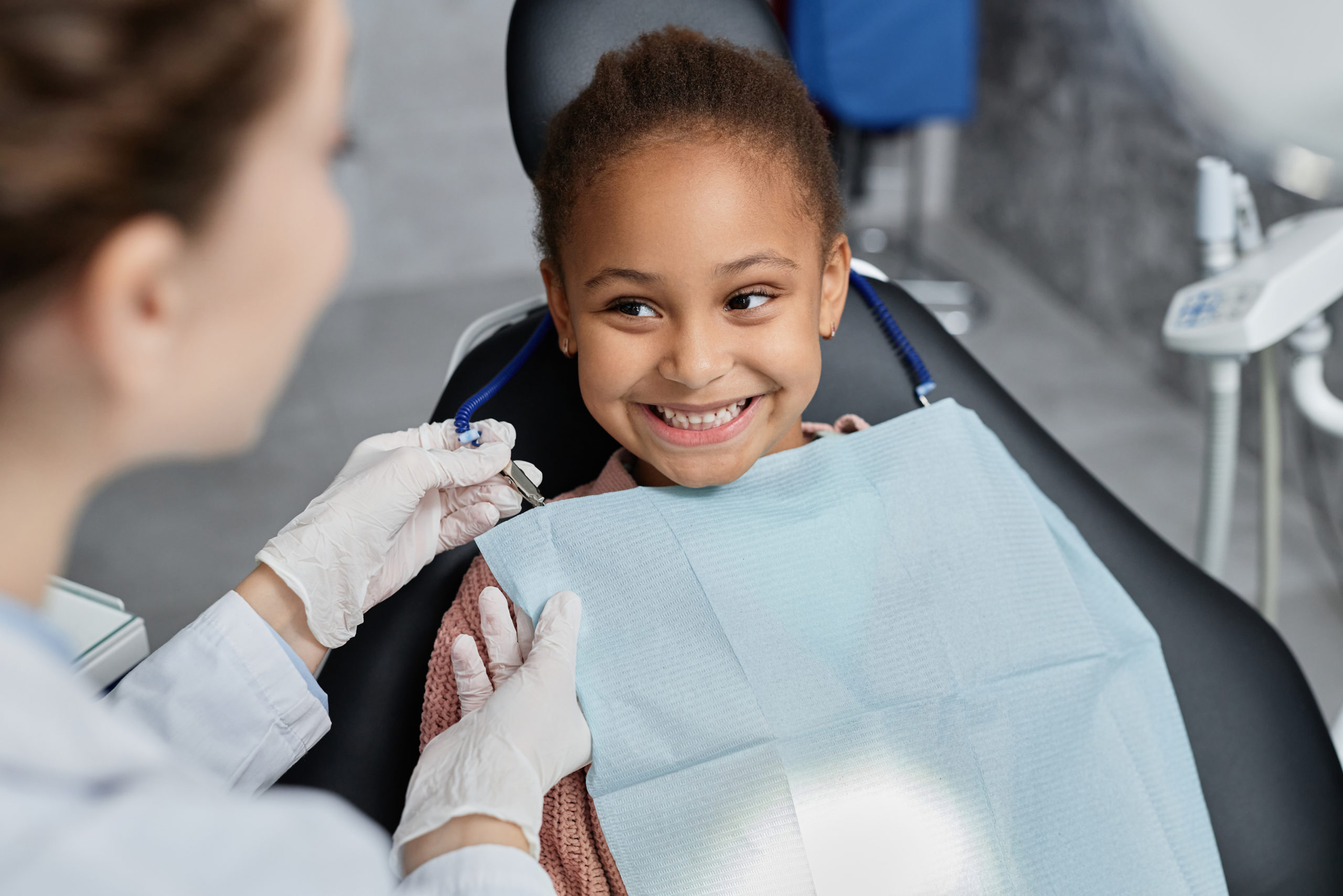 Portrait of smiling little girl in dental chair with nurse preparing her for teeth check up, copy space
